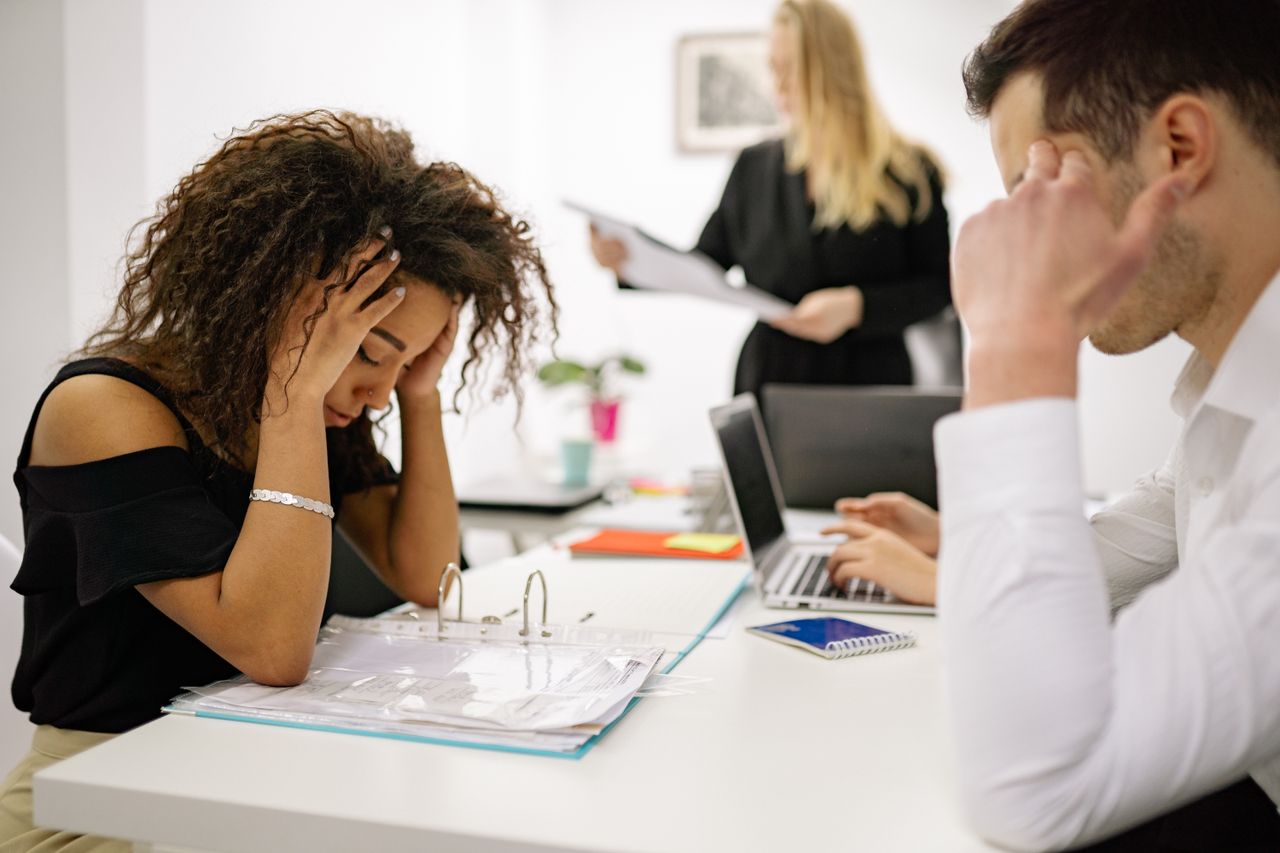 Trabalhadora estressada sentada à mesa de escritório com colegas ao fundo