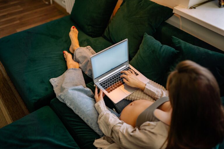 Mulher grávida sentada no sofá trabalhando em um notebook