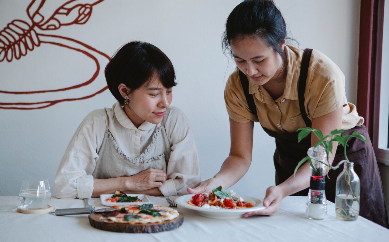 Duas trabalhadoras de avental atendendo em um restaurante