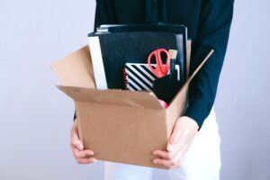 Trabalhadora carregando caixa com pertences após ser demitida antes de completar um ano de empresa