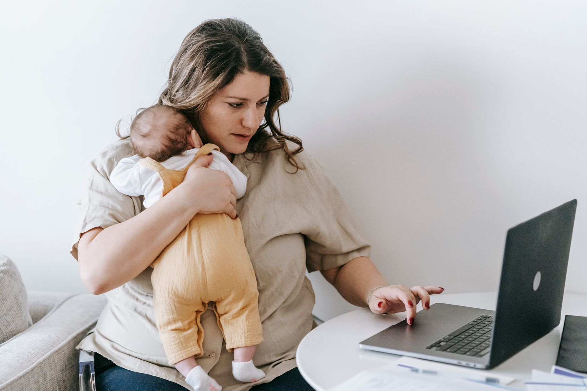 Mãe segurando o filho recém-nascido enquanto trabalha em casa com o notebook