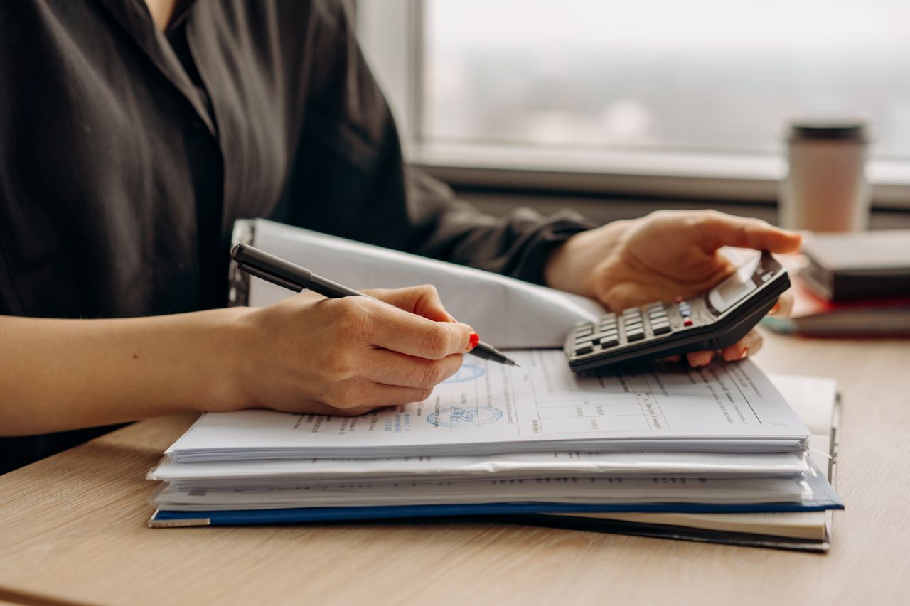 Trabalhadora conferindo cálculos de pagamento com calculadora e documentos sobre a mesa