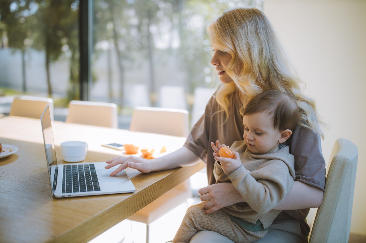 Mulher com criança no colo usando o notebook em uma mesa de madeira