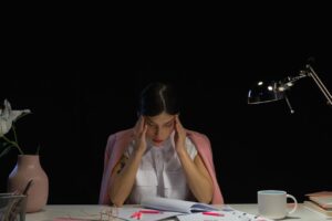 Mulher sentada à mesa de escritório com as mãos na cabeça, aparentando estresse