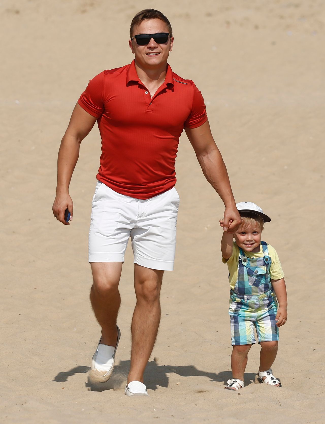 Pai sorrindo caminhando de mãos dadas com o filho pequeno
