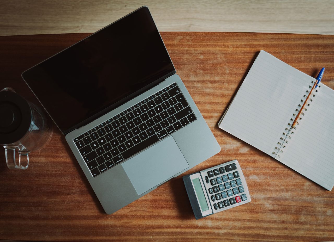 Mesa de trabalho com notebook, calculadora e caderno para conferir cálculos do salário