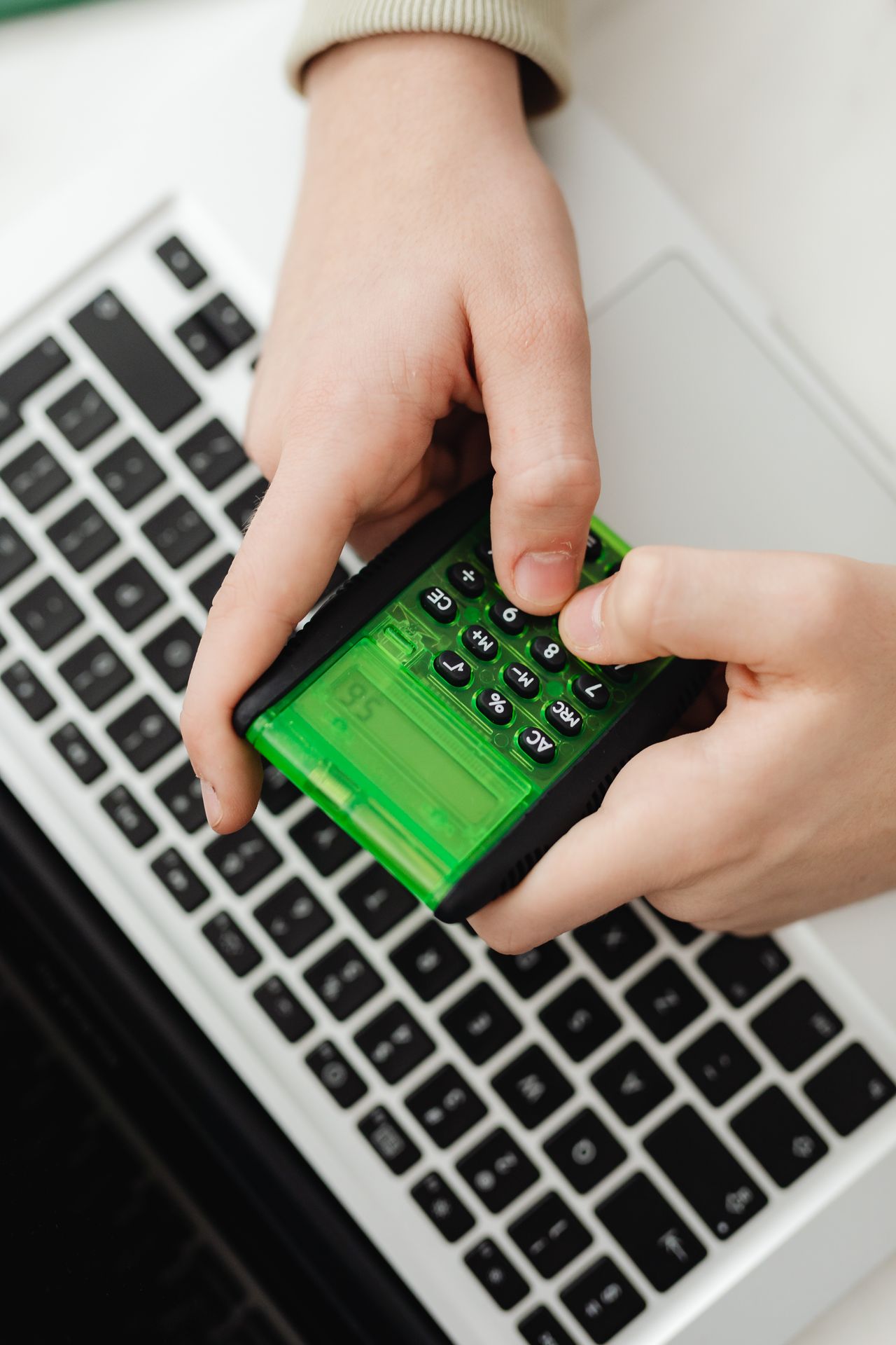 Mãos usando uma calculadora verde sobre o teclado de um notebook