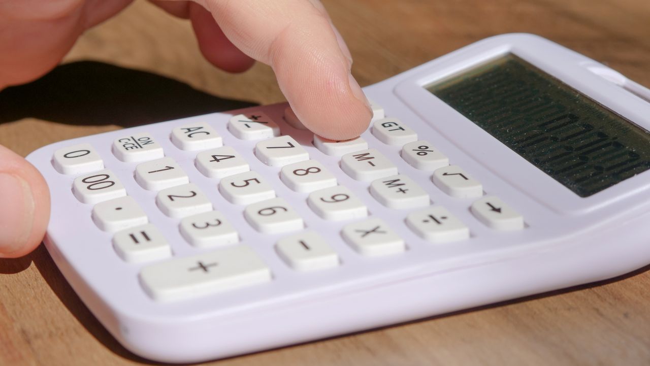 Mão pressionando as teclas de uma calculadora branca sobre uma mesa de madeira