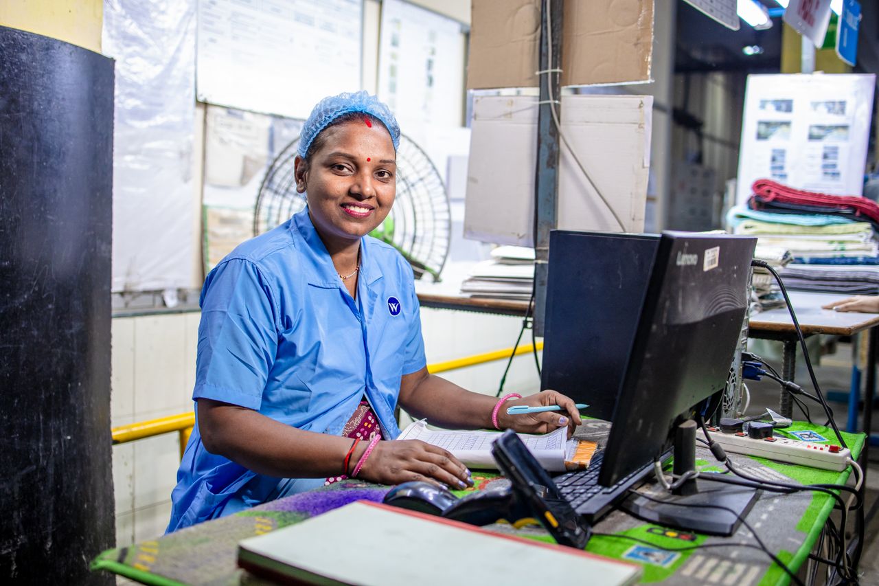 Trabalhadora sorrindo diante do computador em uma fábrica