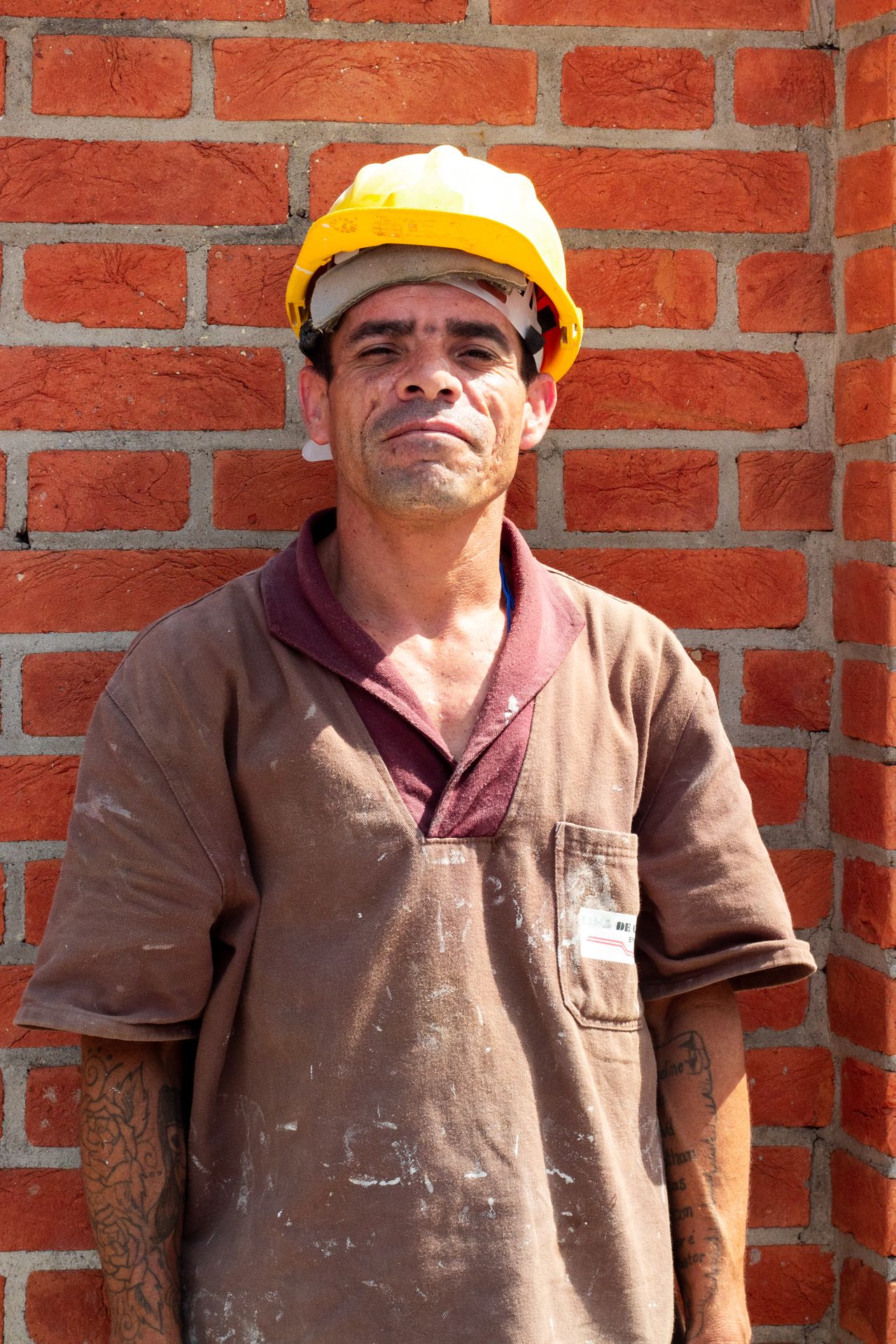Trabalhador de capacete em frente a parede de tijolos