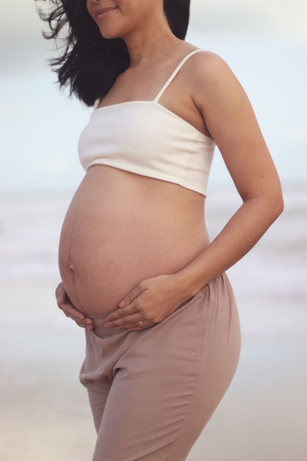 Gestante com as mãos sobre a barriga em uma praia